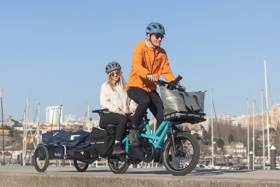 Couple riding a Tern GSD Gen 2 family e-cargo bike while towing a trailer