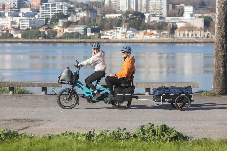 Couple riding the Tern GSD Gen 3 cargo bike while towing a Burley bike trailer.
