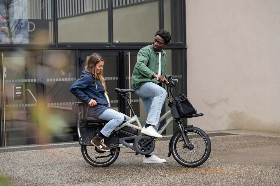 A guy riding a Tern HSD cargo e-bike with a young woman passenger sitting on the rear rack.